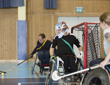 Tre personer spelar rullstolsinnebandy. 